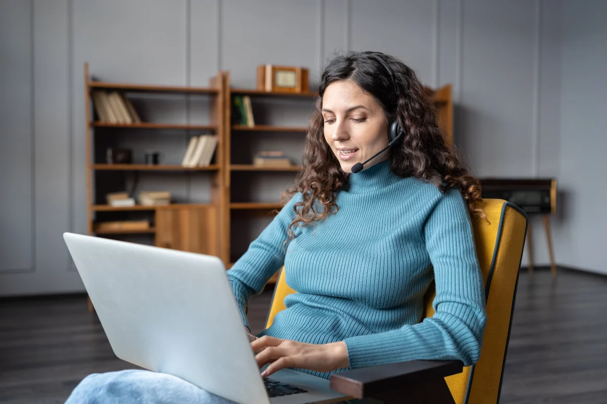 mladá IT žena s mikrofónom sedí v kresle na homeoffice a pracuje na laptope