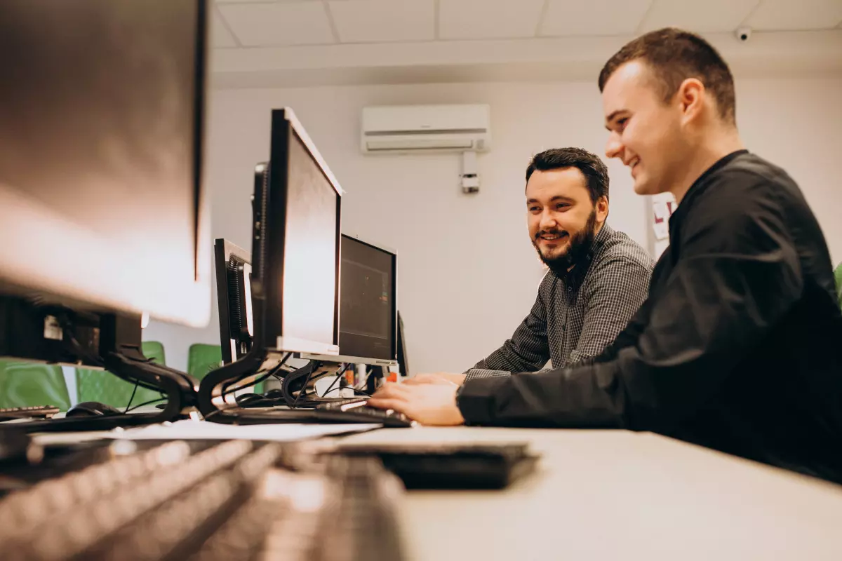 muži programátori pozerajú do monitora a usmievajú sa